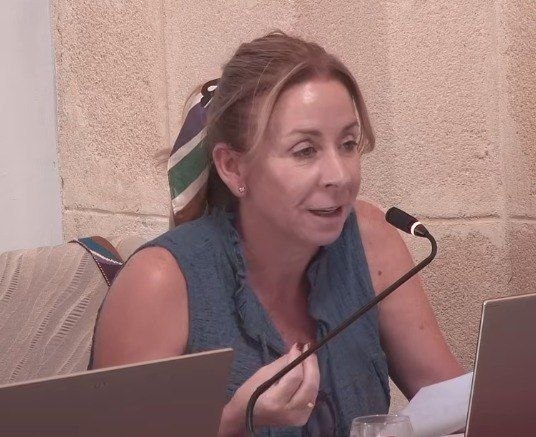 Mujer interviniendo en una reunión, con un micrófono y un ordenador.